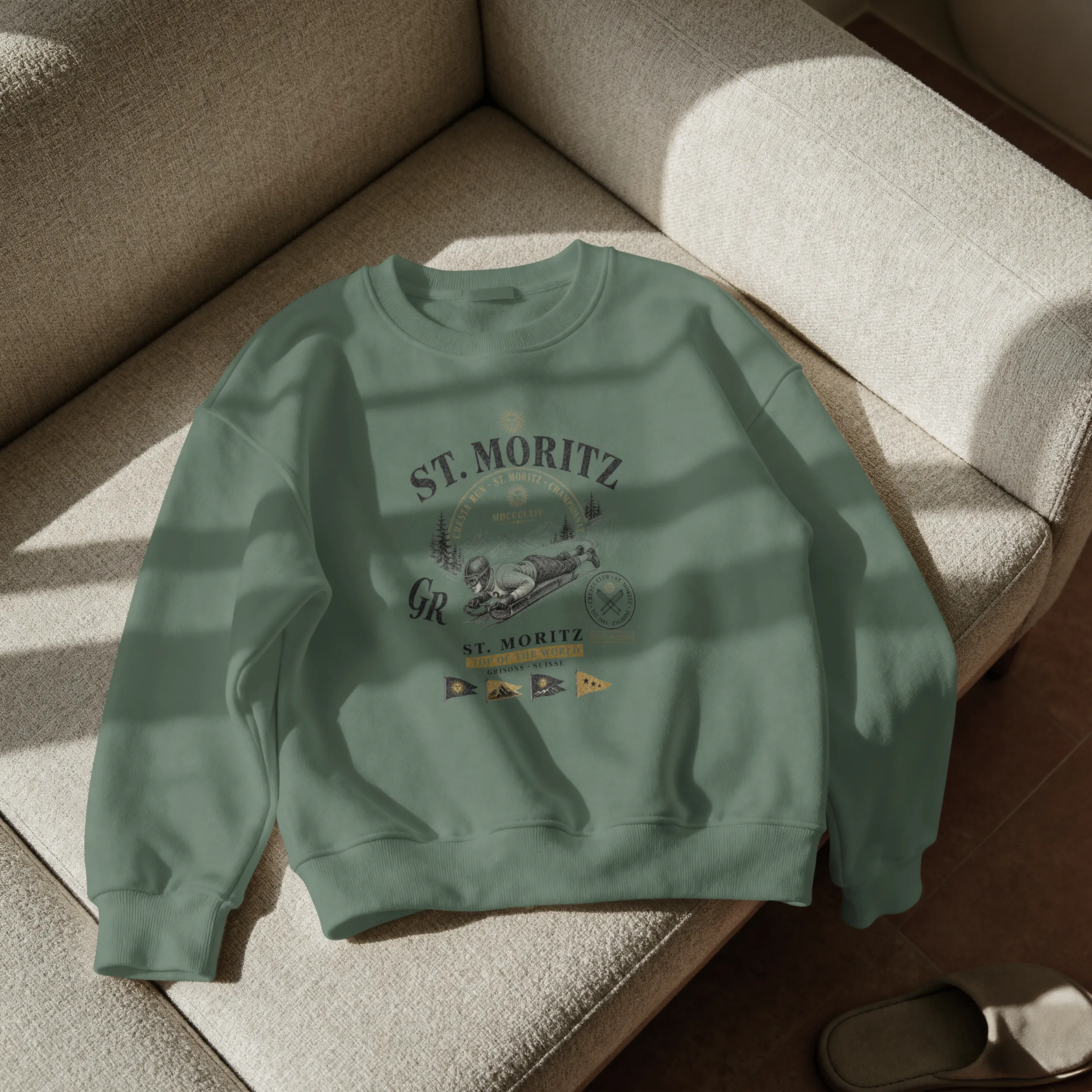 sweat-st-moritz-vintage-vert Sweat St. Moritz vintage vert militaire posé sur canapé, gros plan sur le design rider Cresta Run