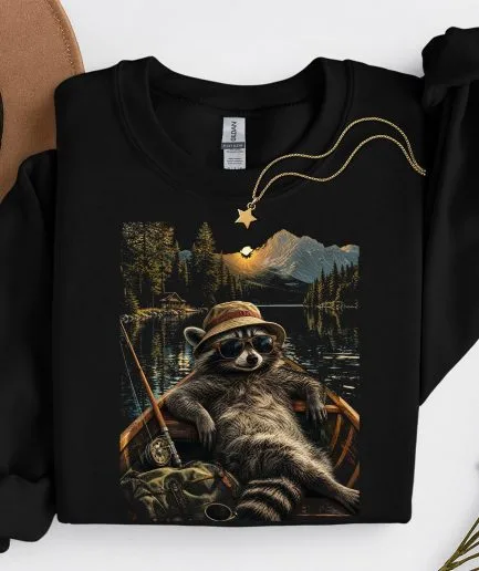 Sweat-shirt noir col rond imprimé raton laveur pêcheur dans une barque sur un lac de montagne, coupe unisexe décontractée.