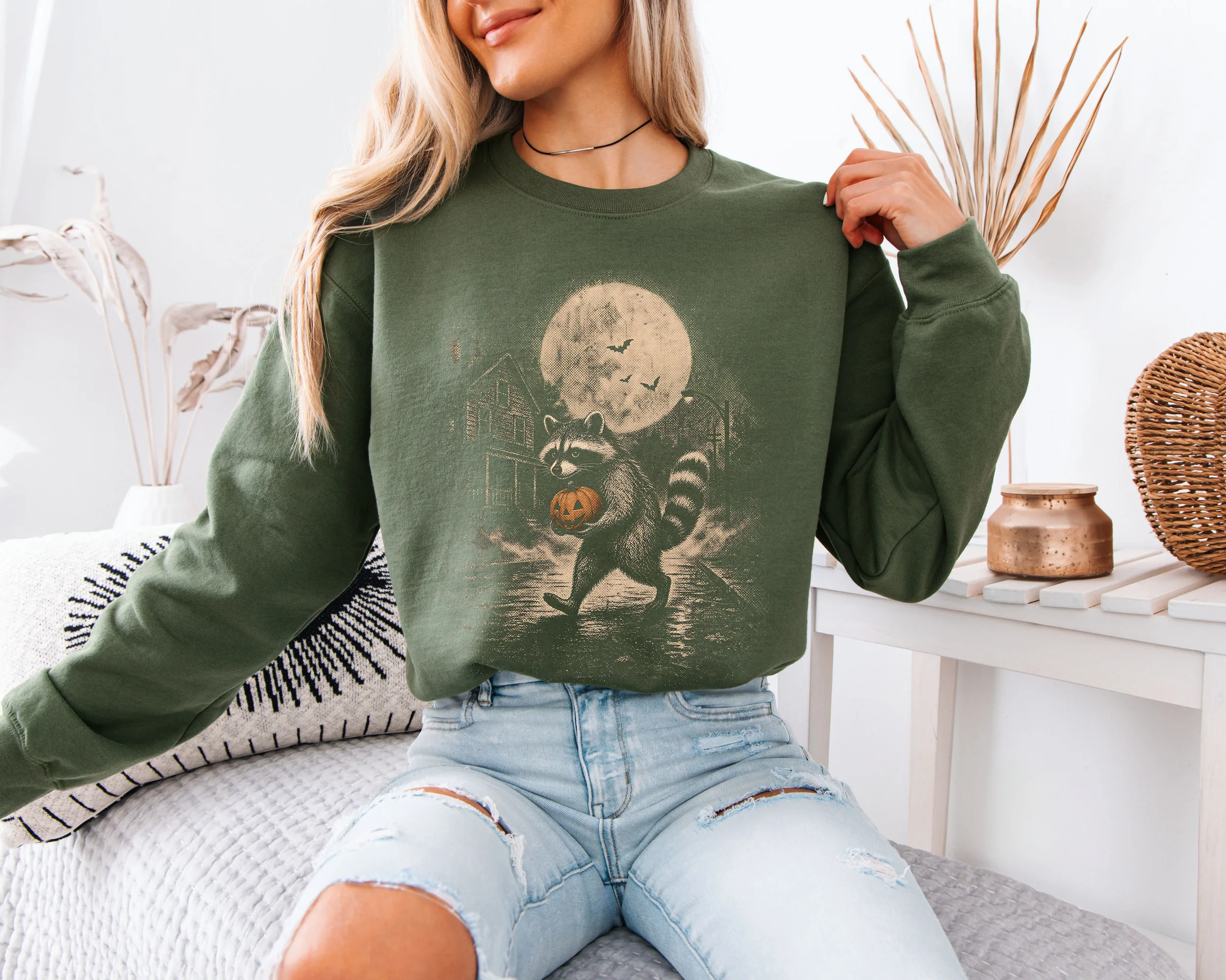 sweat-raton-halloween-militaire Femme portant un sweat Halloween raton laveur vert militaire, maison hantée et pleine lune.