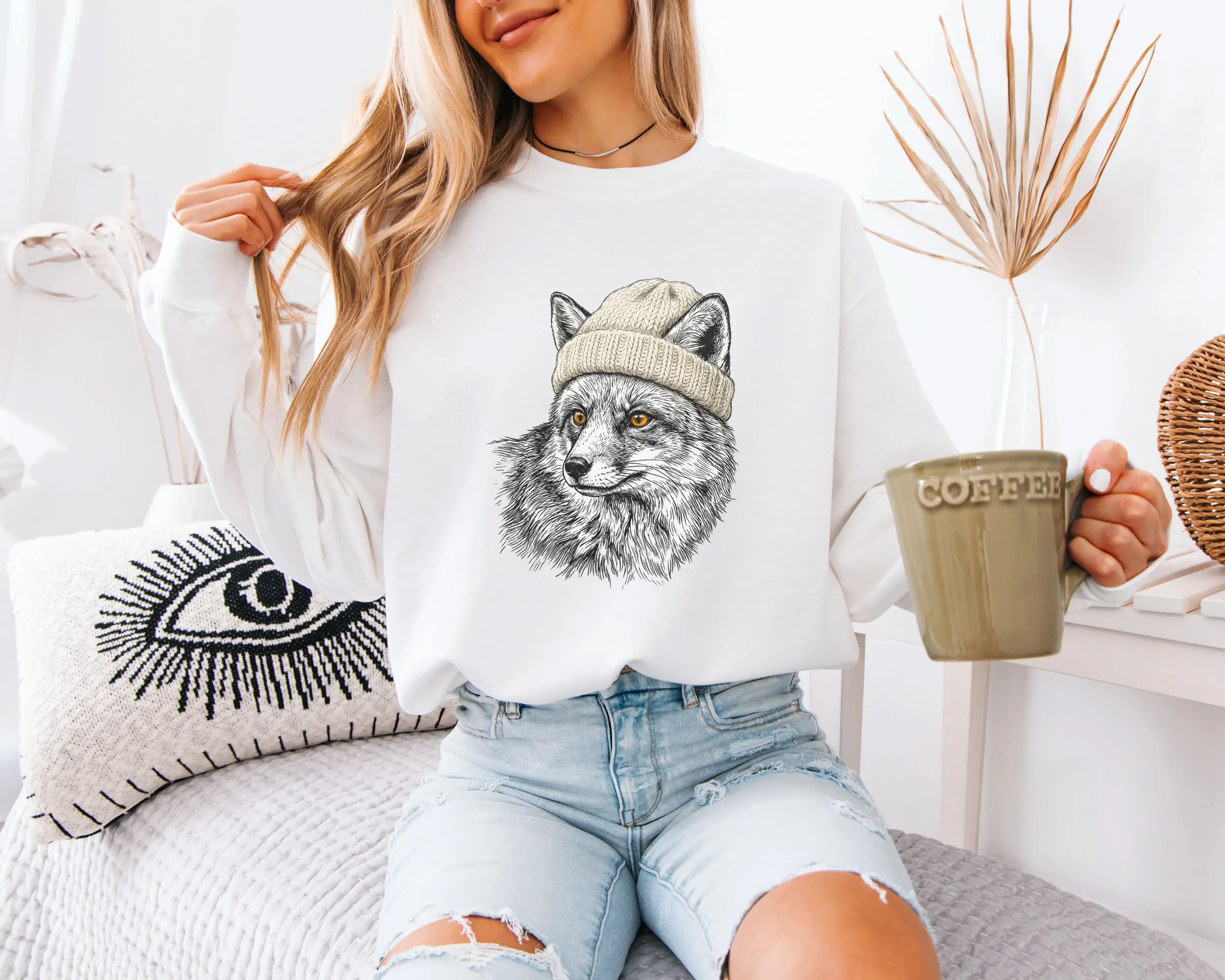sweat-renard-bonnet-blanc-f Femme portant un sweat blanc avec un renard en bonnet illustré au crayon, tasse de café à la main